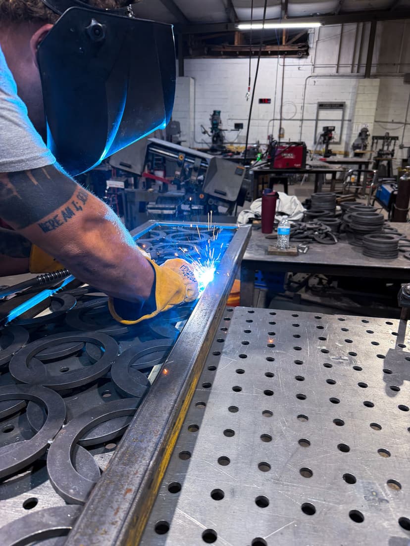 Welding metal pieces in workshop, sparks flying, highlighting craftsmanship and equipment.